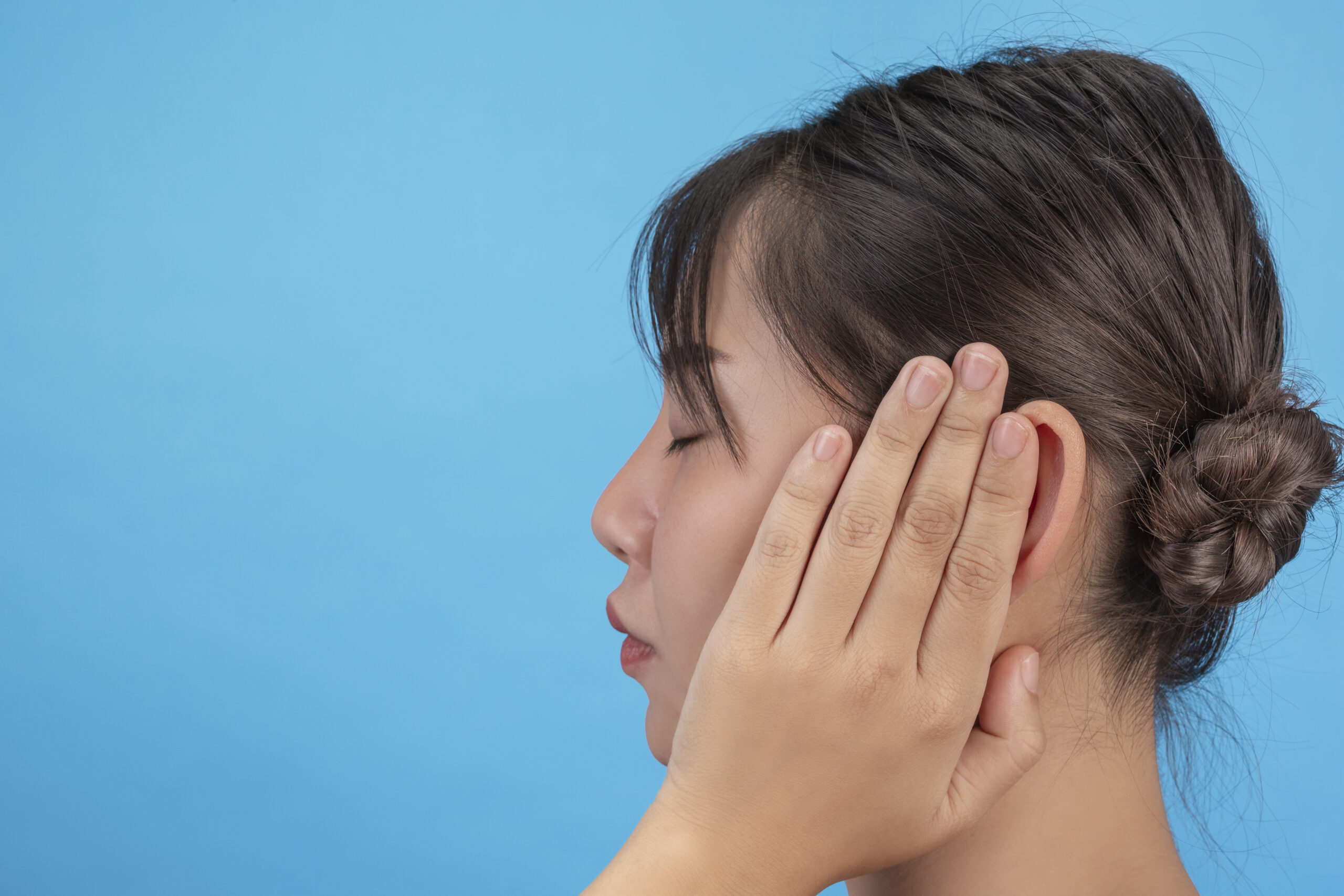 Young girl is unhappy and trying to close the ears with her hands on blue background.